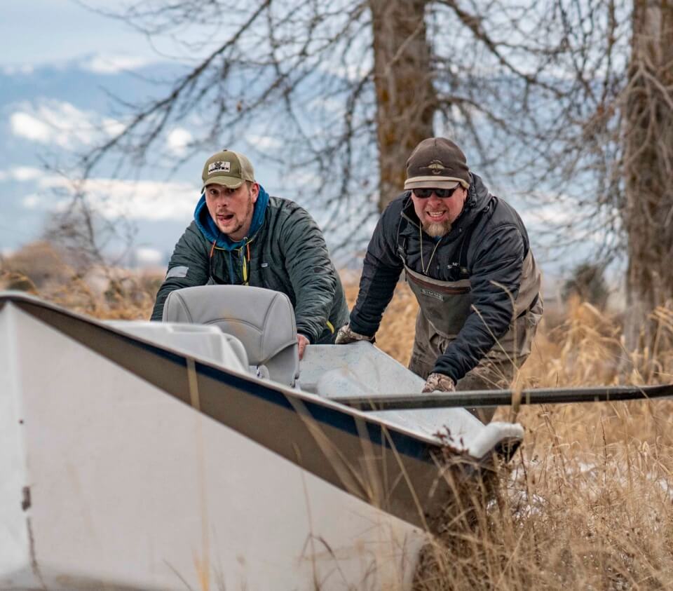 Two people pushing boat into river.