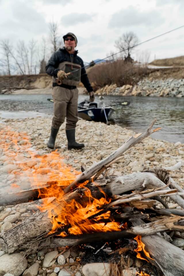 Fisherman in winter fishing near camp fire.